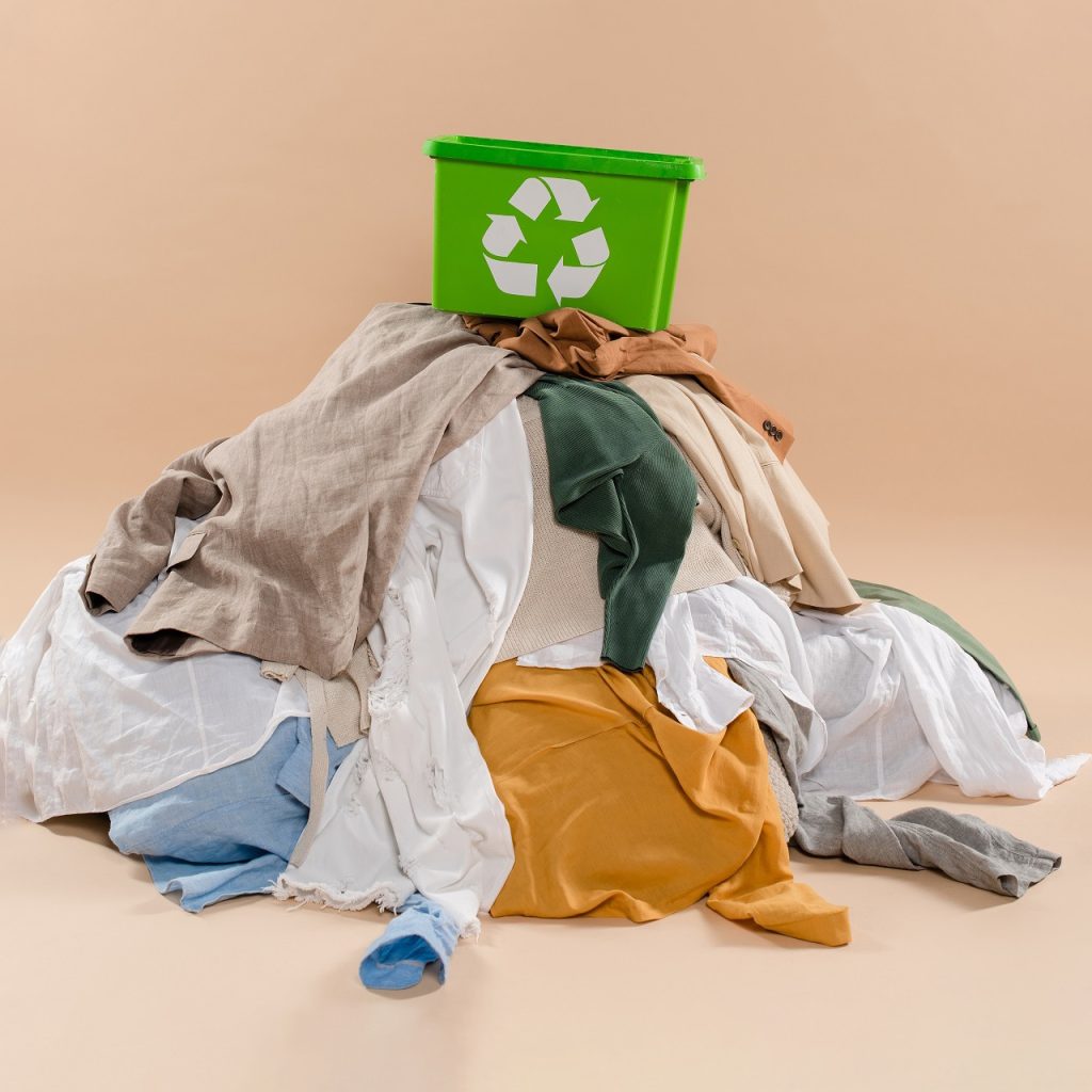 recycling box on stack of clothing on beige background, environm