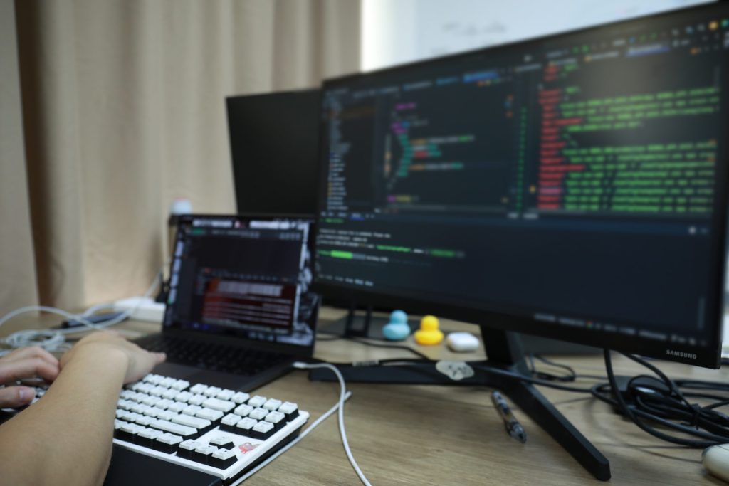 AI-Driven Fashion Design - Revolutionizing the Industry with Technology A coder working on a laptop and monitor, symbolizing AI-driven design and technology in the fashion industry.