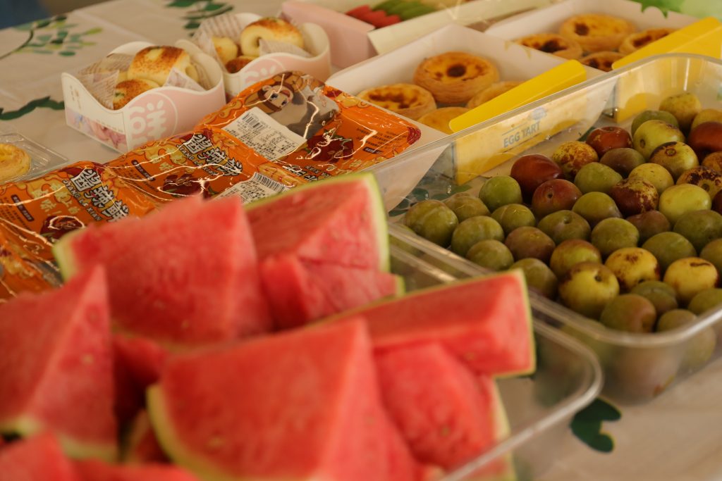 Watermelon and Snacks at D&J Fashion’s Birthday Celebration A table with watermelon, egg tarts, and various snacks at D&J Fashion’s July birthday celebration.