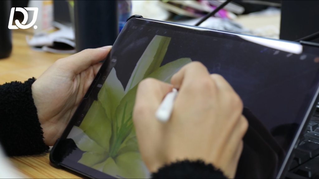 Designer using a stylus to draw a green leaf pattern on a tablet.