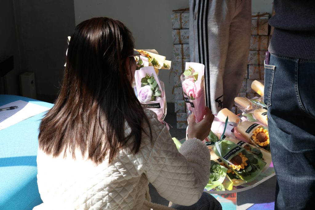 An employee chooses a handmade flower bouquet during a Women’s Day celebration at D&J Fashion, showing a people-first company culture, employee well-being, ethical workplace practices, and corporate responsibility inside a women’s apparel manufacturer and OEM ODM supplier in China.