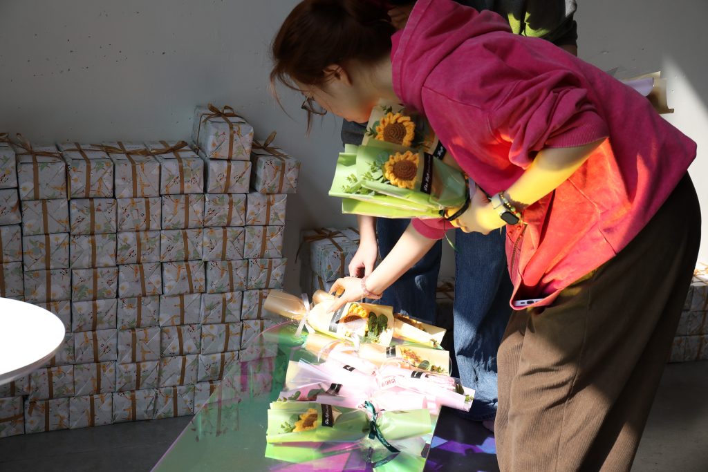 An employee receives multiple handmade sunflower bouquets during a company celebration, representing employee well-being, ethical workplace practices, and people-first company culture at D&J Fashion sustainable apparel, a women’s clothing factory and apparel export China supplier.